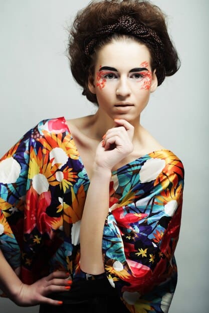 A close-up shot of a woman smiling confidently, wearing a vibrant and eclectic outfit that includes a mix of patterns, textures, and colors. The image emphasizes her bold and playful personal style.