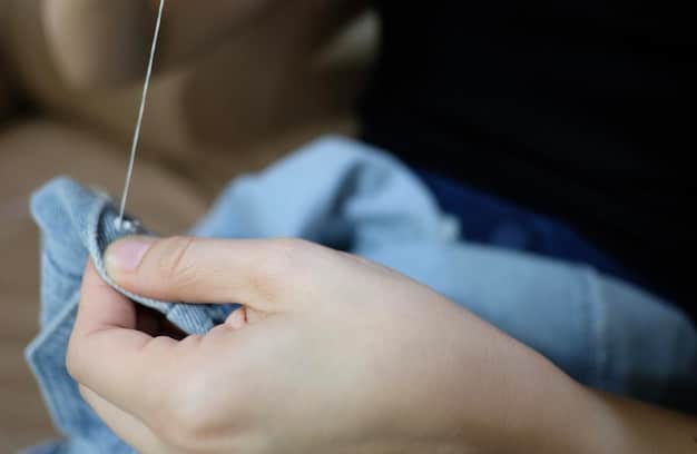 A close-up shot of a person's hands carefully sewing or mending a piece of clothing, showcasing the value of craftsmanship and sustainable fashion practices as an alternative to fast fashion. The image highlights the importance of preserving traditional skills.