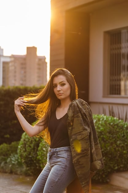 A woman with medium-length bronde hair, styled in loose waves, standing in a sunlit urban environment.