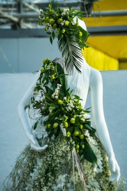 A model wearing a dress made of sustainable materials on a runway. The dress is designed with earthy tones, natural dyes, and minimalist designs, reflecting a connection to nature and a commitment to environmental responsibility. Background includes green plants and soft lighting.